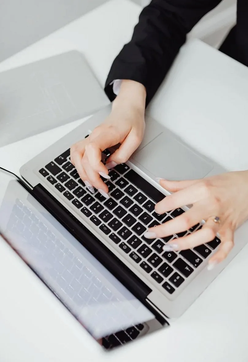 Hands typing on a laptop keyboard on a white desk