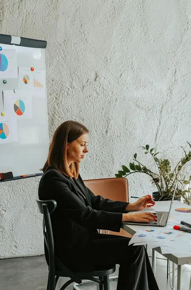 Woman working at a desk next to a wall of charts