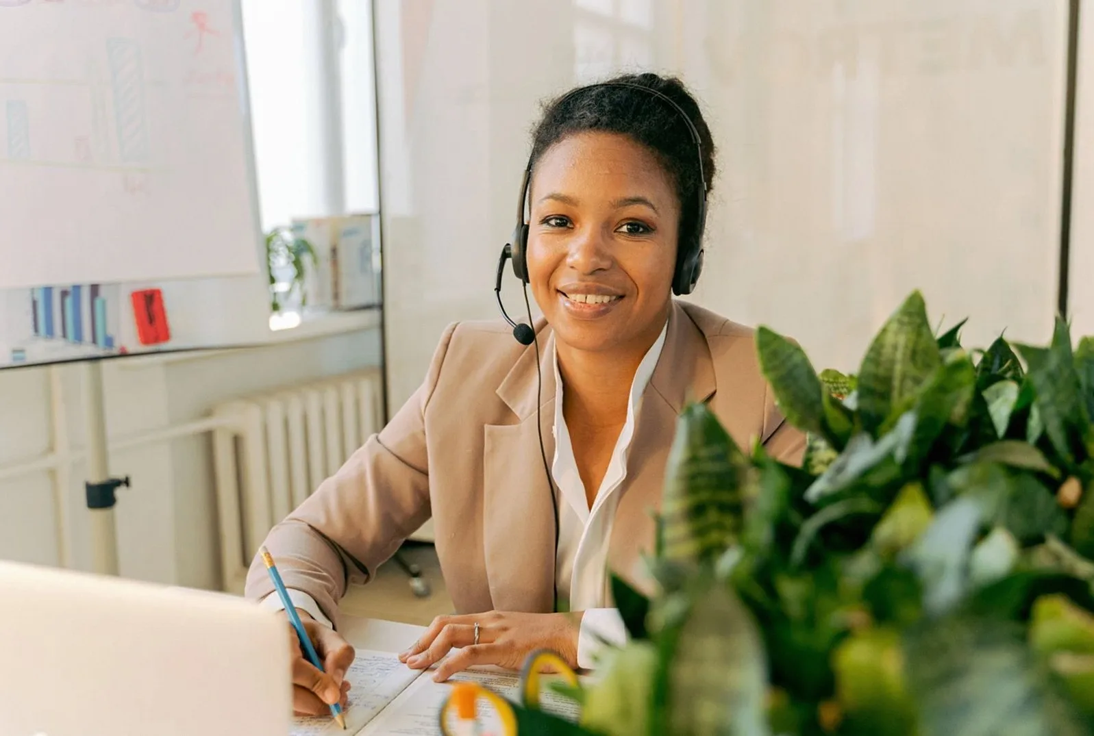 Smiling woman with a headset at a desk beside a plant