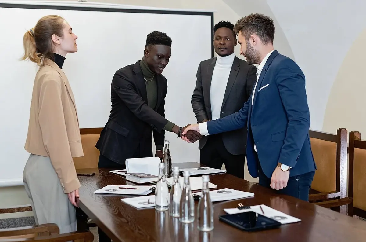 Four professionals around a conference table, two of them shaking hands